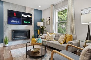 Un salon avec une cheminée, un canapé agrémenté de coussins à motifs, une table basse et un téléviseur fixé au mur, qui affiche les logos de différents services de diffusion en continu.