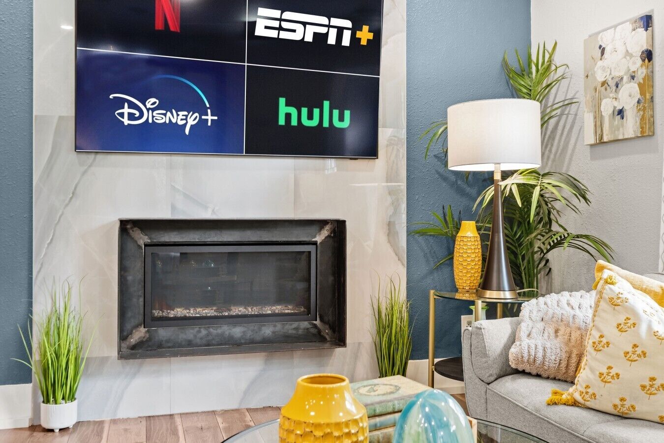 Een woonkamer met een open haard, een televisie erboven met logo's, en een bank met decoratieve kussens.