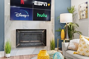 Ein Wohnzimmer mit Kamin, einem darüber montierten Fernseher mit Logos und einer Couch mit dekorativen Kissen.