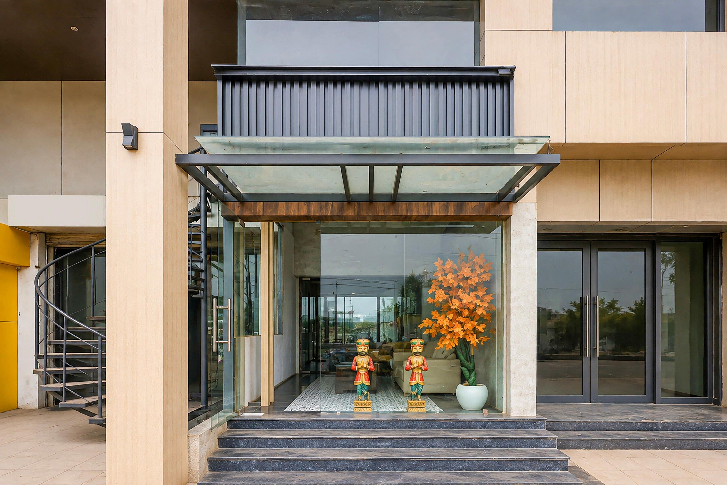 A modern building entrance with a glass door, a staircase, and a decorative plant.
