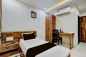 Una habitación de hotel con cama, mesita de noche, lámpara, escritorio, silla y un equipo de aire acondicionado.