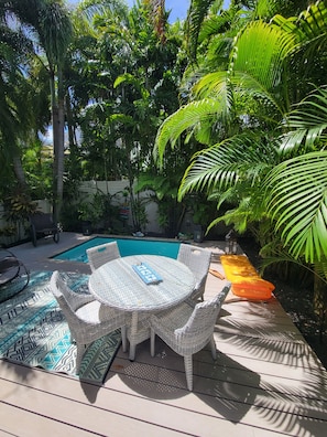 A poolside area with a round table and chairs, surrounded by lush tropical foliage. - Sunset Serenity-Minutes away from the beaches, Old Town and the best of KW! (Key West)