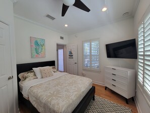 A bedroom with a bed, a television, a dresser, a window with blinds, and a door. - Sunset Serenity-Minutes away from the beaches, Old Town and the best of KW! (Key West)