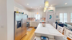 A modern kitchen with white cabinetry, a stainless steel refrigerator, and a central island with a bowl. - Sunset Serenity-Minutes away from the beaches, Old Town and the best of KW! (Key West)