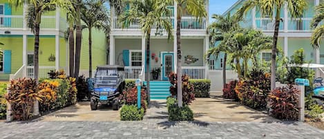 A multi-story hotel with a paved driveway, palm trees, and a blue vehicle parked in front.