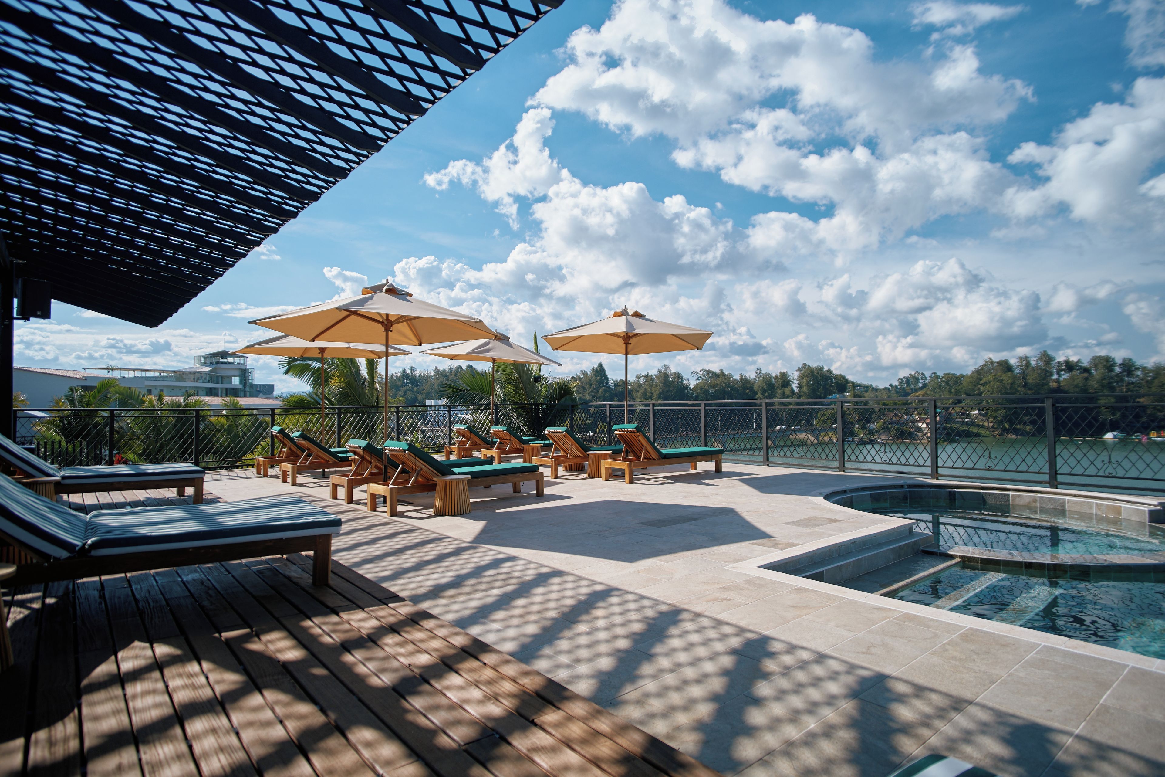 A poolside area with lounge chairs and umbrellas, a pool, and a view of the sky and clouds.