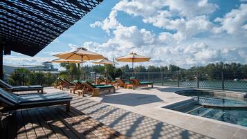 A poolside area with lounge chairs and umbrellas, a pool, and a view of the sky and clouds.