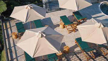 Una terraza en la azotea con varias zonas de descanso, cada una con una mesa y una silla, y varios sombrillas grandes que brindan sombra.