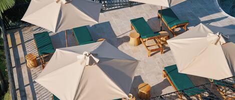 A rooftop terrace with multiple lounge areas, each with a table and chair, and several large umbrellas providing shade.