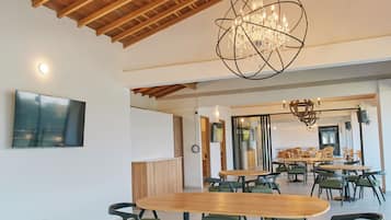 Un comedor amplio con mesas y sillas de madera, un candelabro y un televisor montado en la pared.