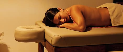 A person lying on a massage table in a room with a wooden floor and a plain wall.