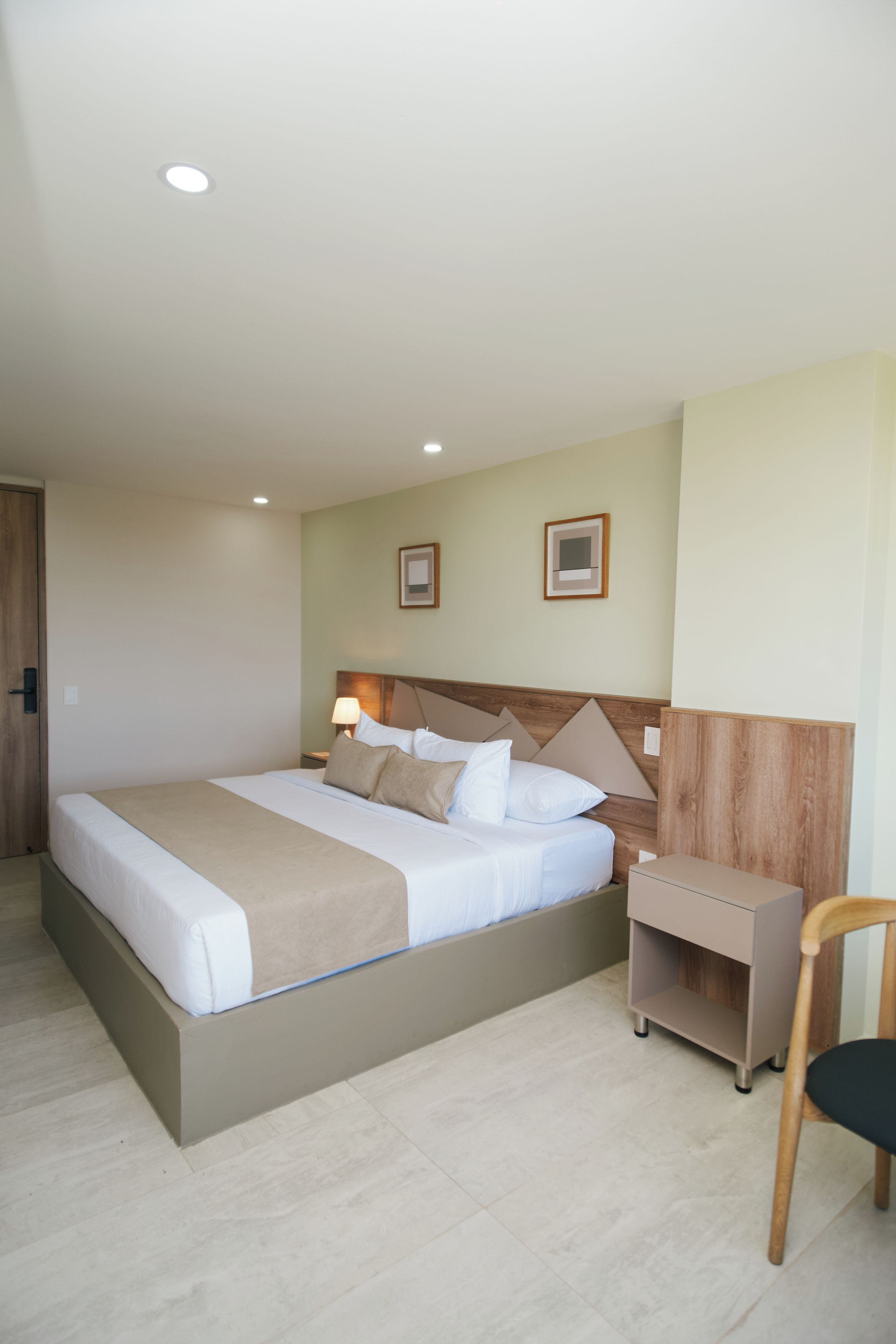 Una habitación de hotel con una cama grande, mesitas de noche, una silla y un tocador.