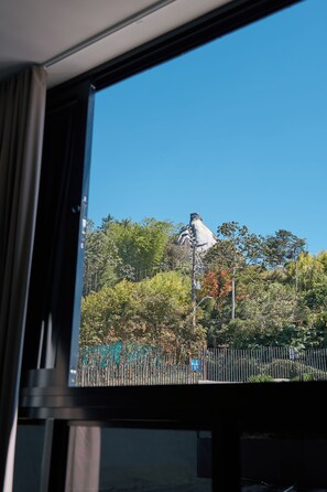 Vista a través de una ventana que muestra un edificio con una estatua en una colina, rodeada de árboles y una cerca.