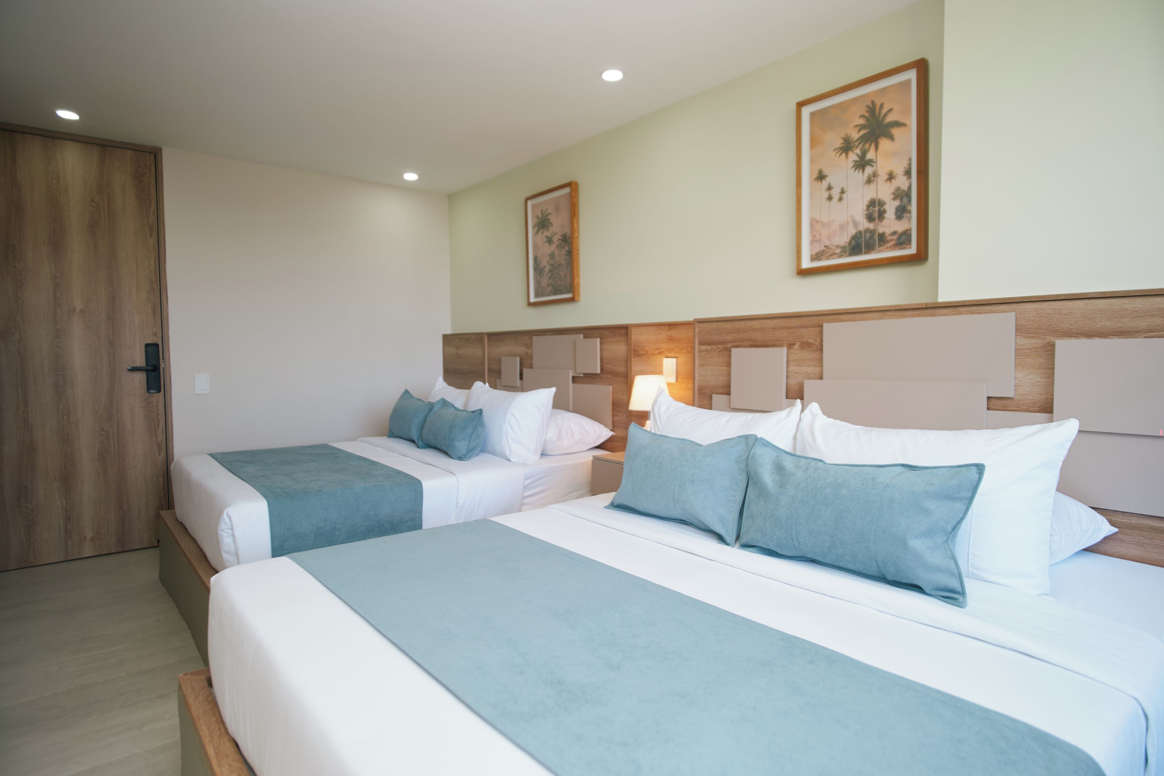 A hotel room with two beds, a wooden door, and a painting on the wall.