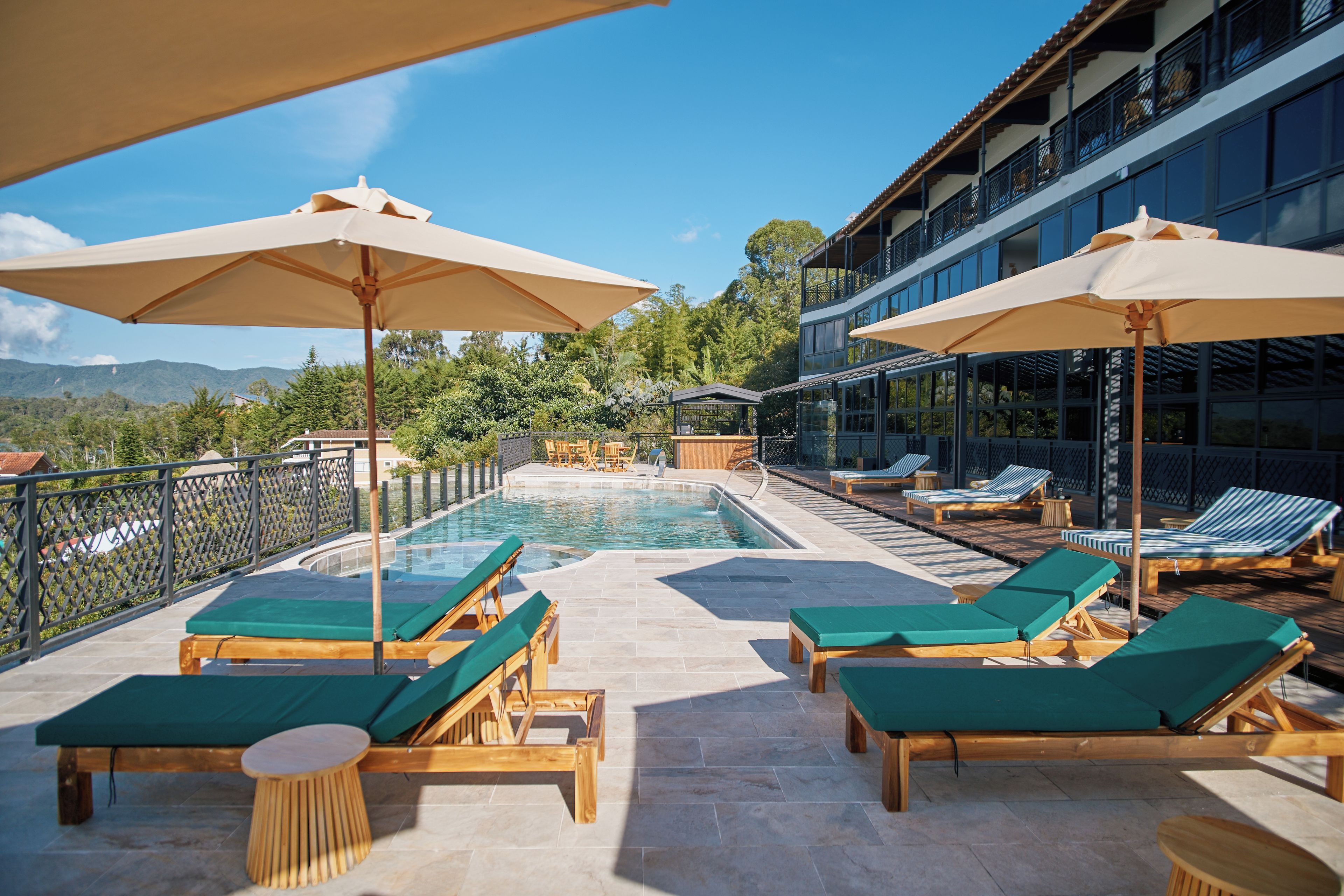 Un espace aménagé au bord de la piscine, avec des chaises longues et des parasols, une piscine et une vue sur les montagnes.