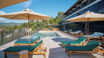 Un espace aménagé au bord de la piscine, avec des chaises longues et des parasols, une piscine et une vue sur les montagnes.