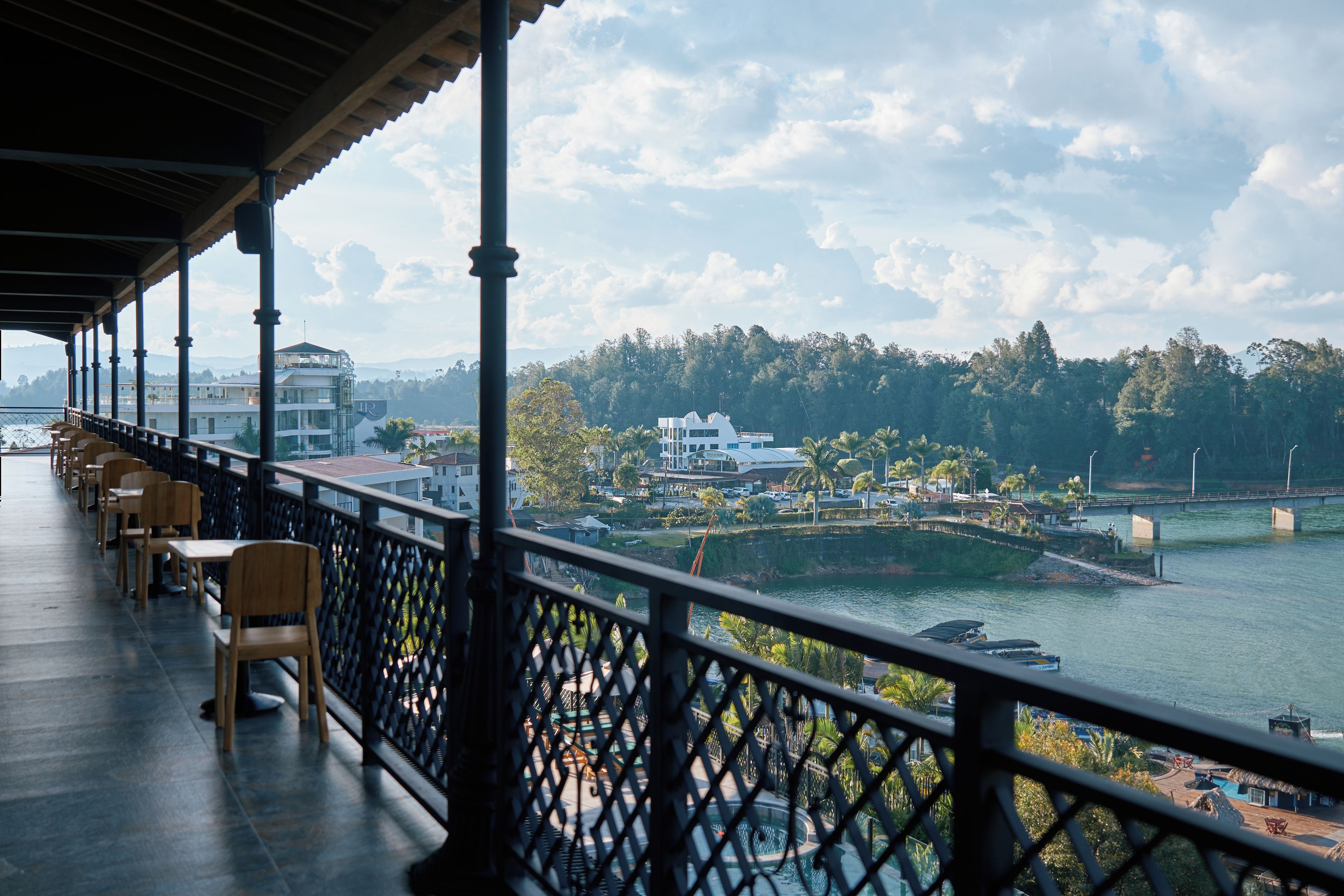 A balcony with chairs overlooking a river, a bridge, and buildings in the distance.