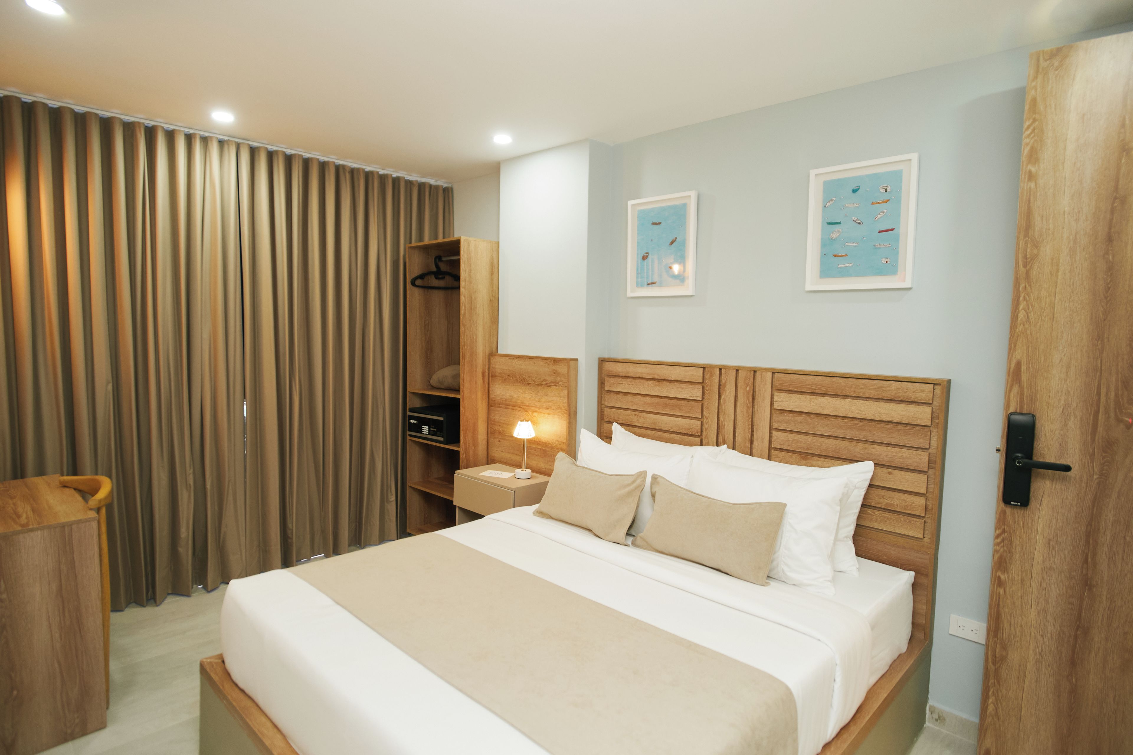 A hotel room with a wooden headboard, a bed with white linens, a bedside table with a lamp, and a wardrobe.