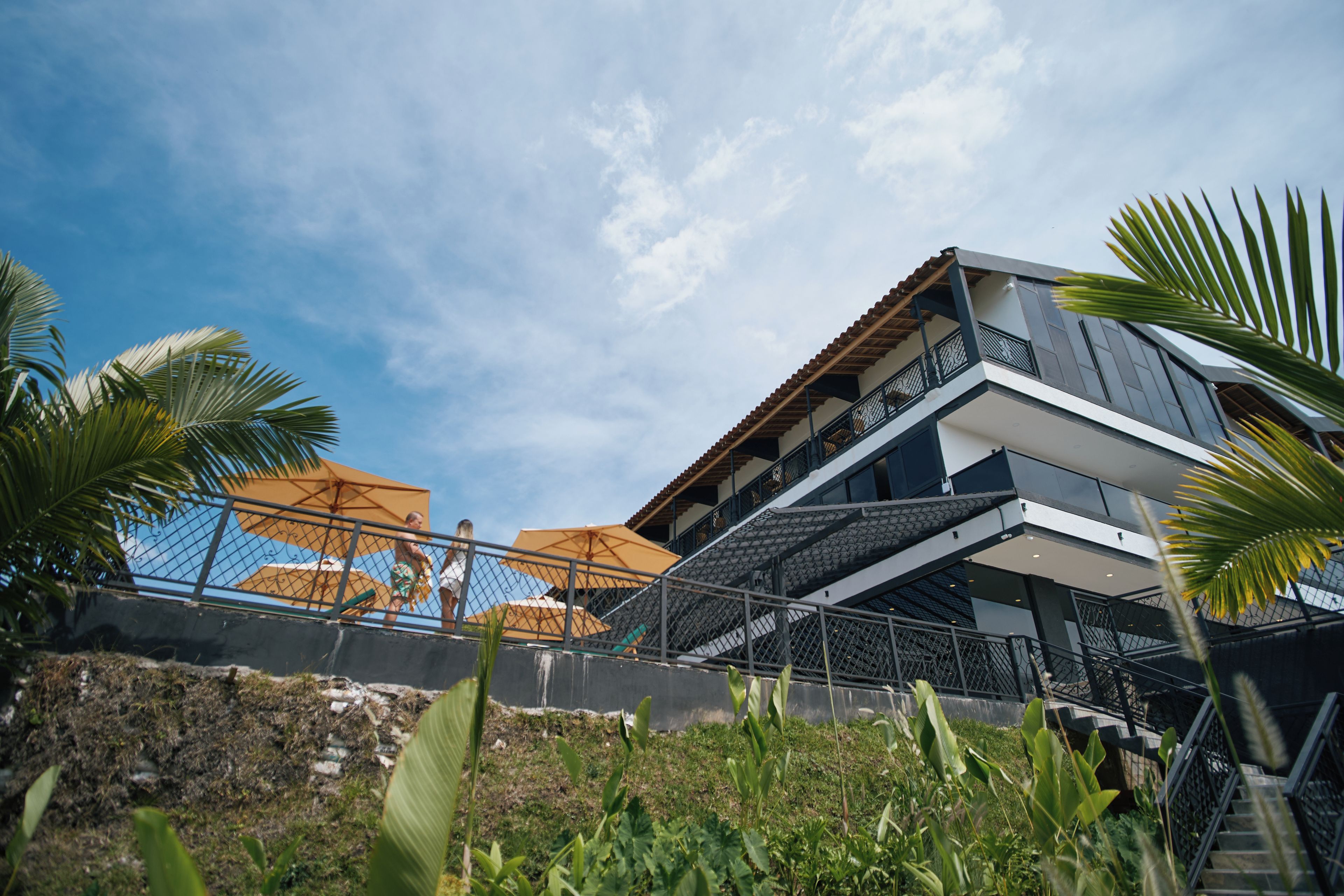 Een modern gebouw met een balkon, buiten parasols en een trap erheen.