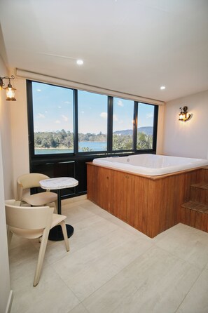 A modern bathroom with a large window, a wooden bathtub, and a small table with chairs.