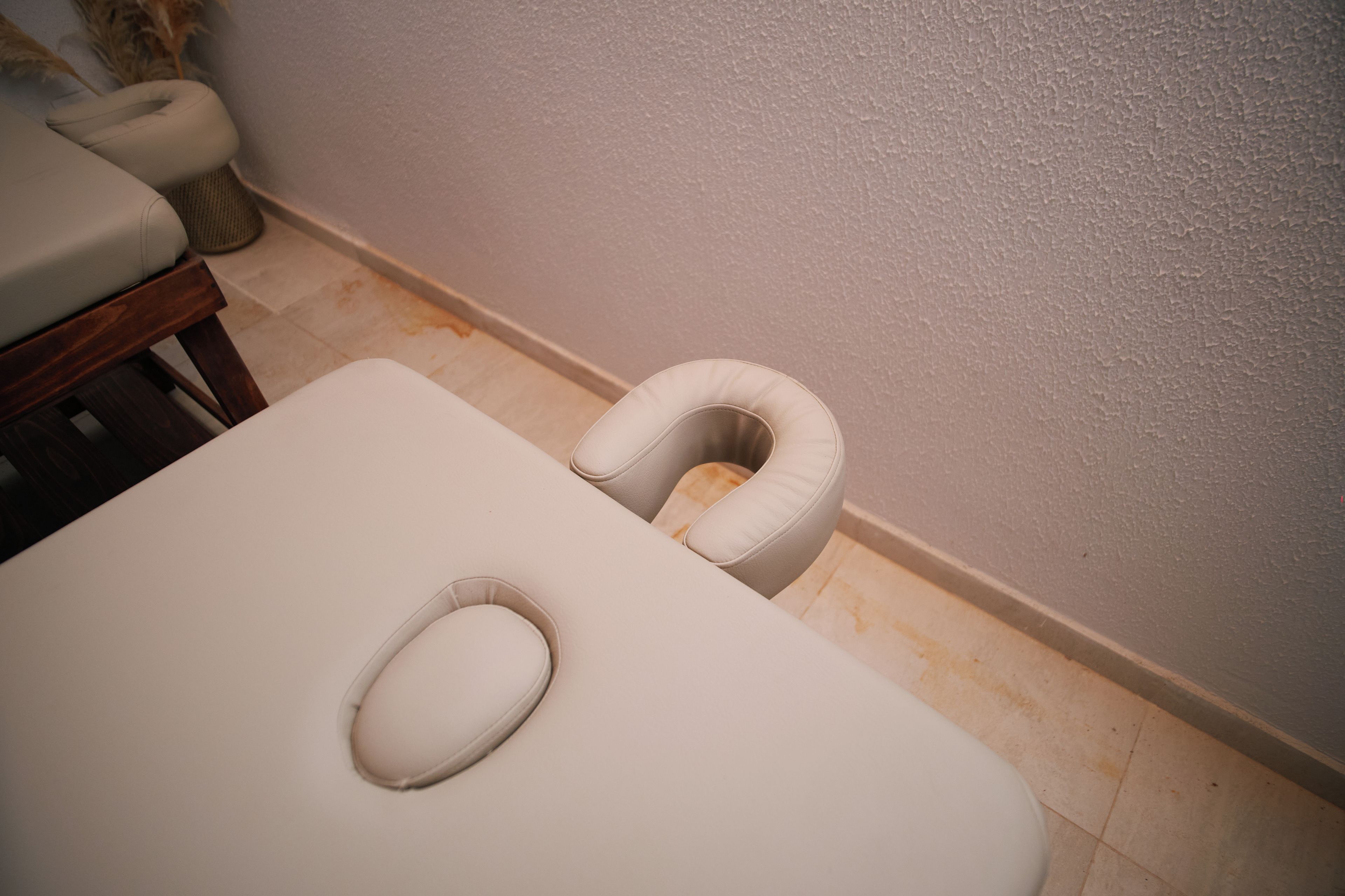 A room with a white examination table, a white cushioned headrest, and a wooden bench.