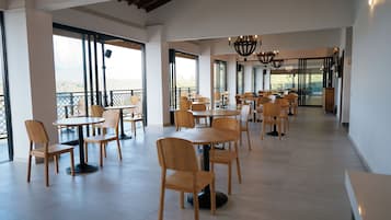 Un espacio interior amplio con varias mesas y sillas, ventanas grandes y un techo alto.