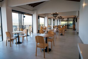 A spacious indoor area with multiple tables and chairs, large windows, and a high ceiling.