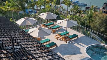 A rooftop pool area with lounge chairs and umbrellas, overlooking a marina with boats.