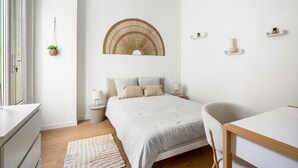 A minimalist bedroom with a bed, bedside tables, a hanging plant, and a wall-mounted shelf. - Le Foch - Bel appt moderne à 20 min de la plage (Béziers)