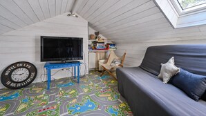 A cozy room with a television, a blue table, a sofa, and a window. - Les Muguets - Maison familiale à 5 min de la plage (Sainte Brevin-les-Pins)