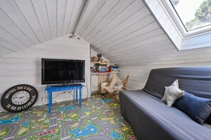 Ett mysigt rum med en tv, ett blått bord, en soffa och ett fönster.