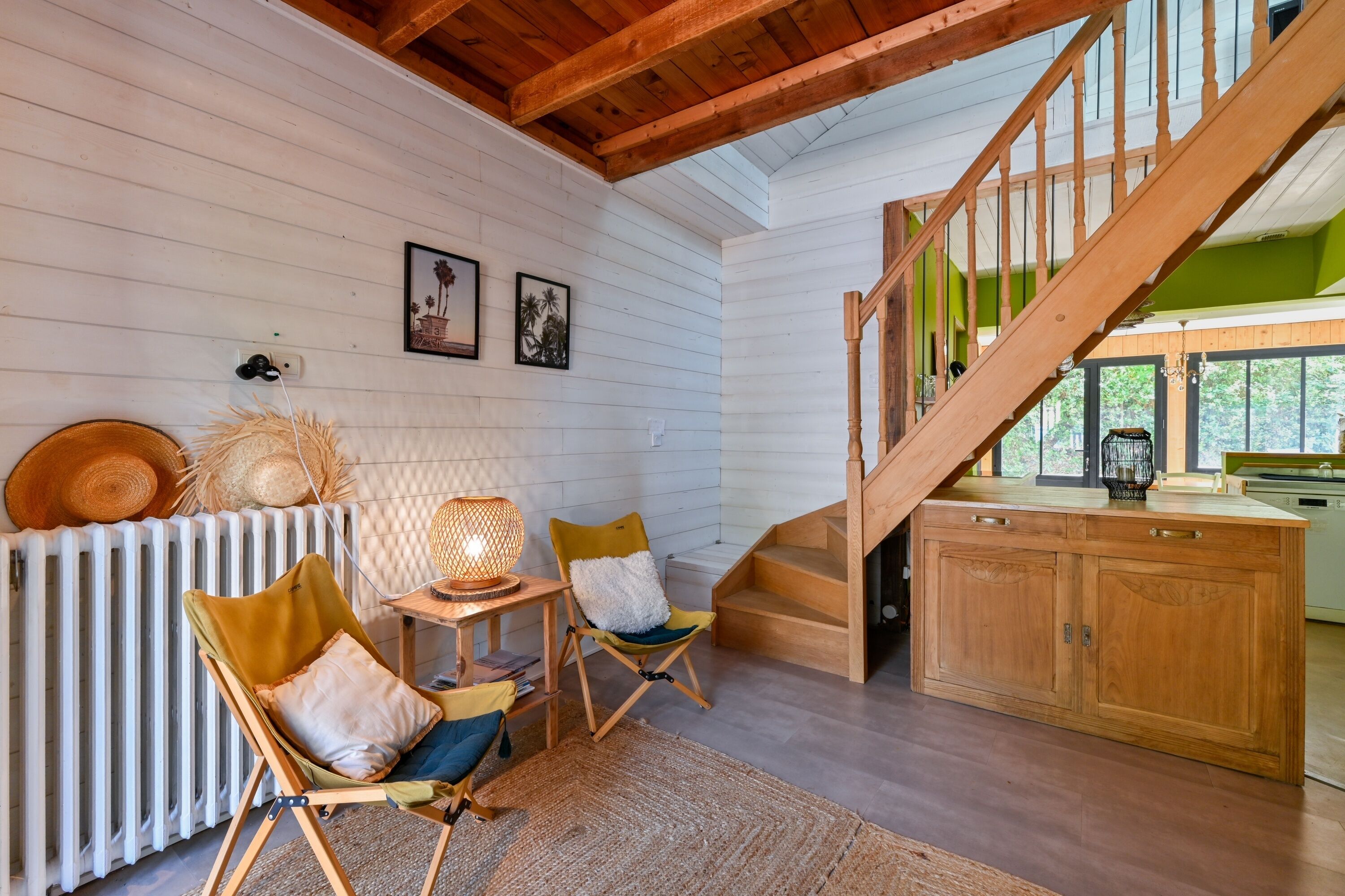 A cozy interior with a wooden staircase, a dining area with chairs and a table, and a kitchen area with cabinets.
