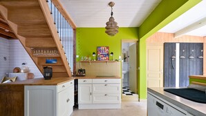 A kitchen with a wooden staircase, a hanging light fixture, and a colorful poster on the wall. - Les Muguets - Maison familiale à 5 min de la plage (Sainte Brevin-les-Pins)