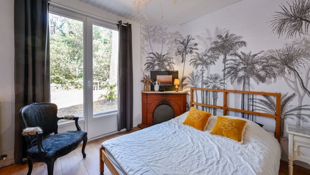A bedroom with a bed, a chair, a TV, and a mural of palm trees. - Les Muguets - Maison familiale à 5 min de la plage (Sainte Brevin-les-Pins)