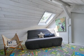 A room with a sloped ceiling, a skylight, a sofa with pillows, a chair, and a colorful floor mat. - Les Muguets - Maison à 5 min de la plage (Sainte Brevin-les-Pins)