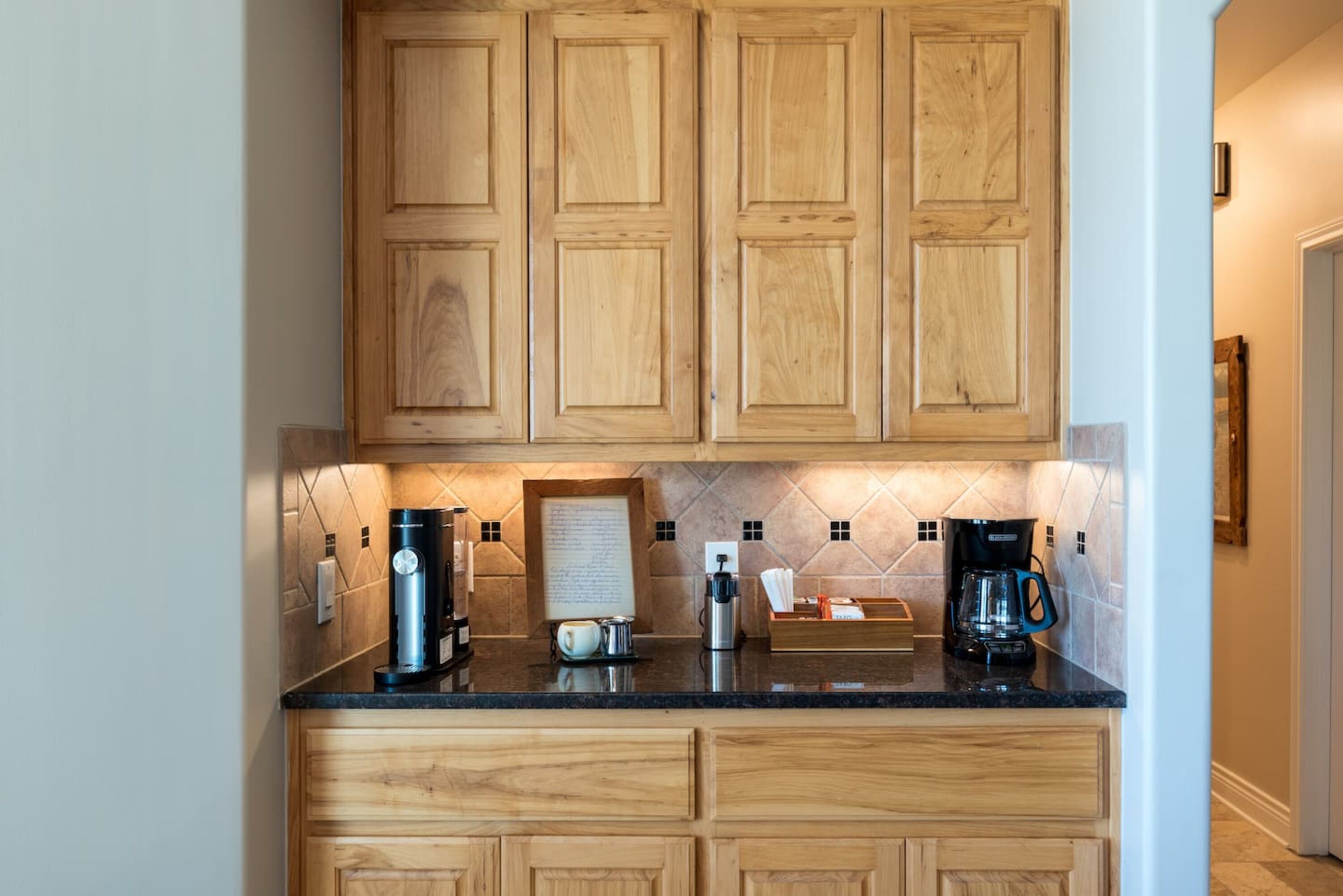 A kitchen with wooden cabinets, a marble backsplash, and a coffee station with multiple coffee makers.