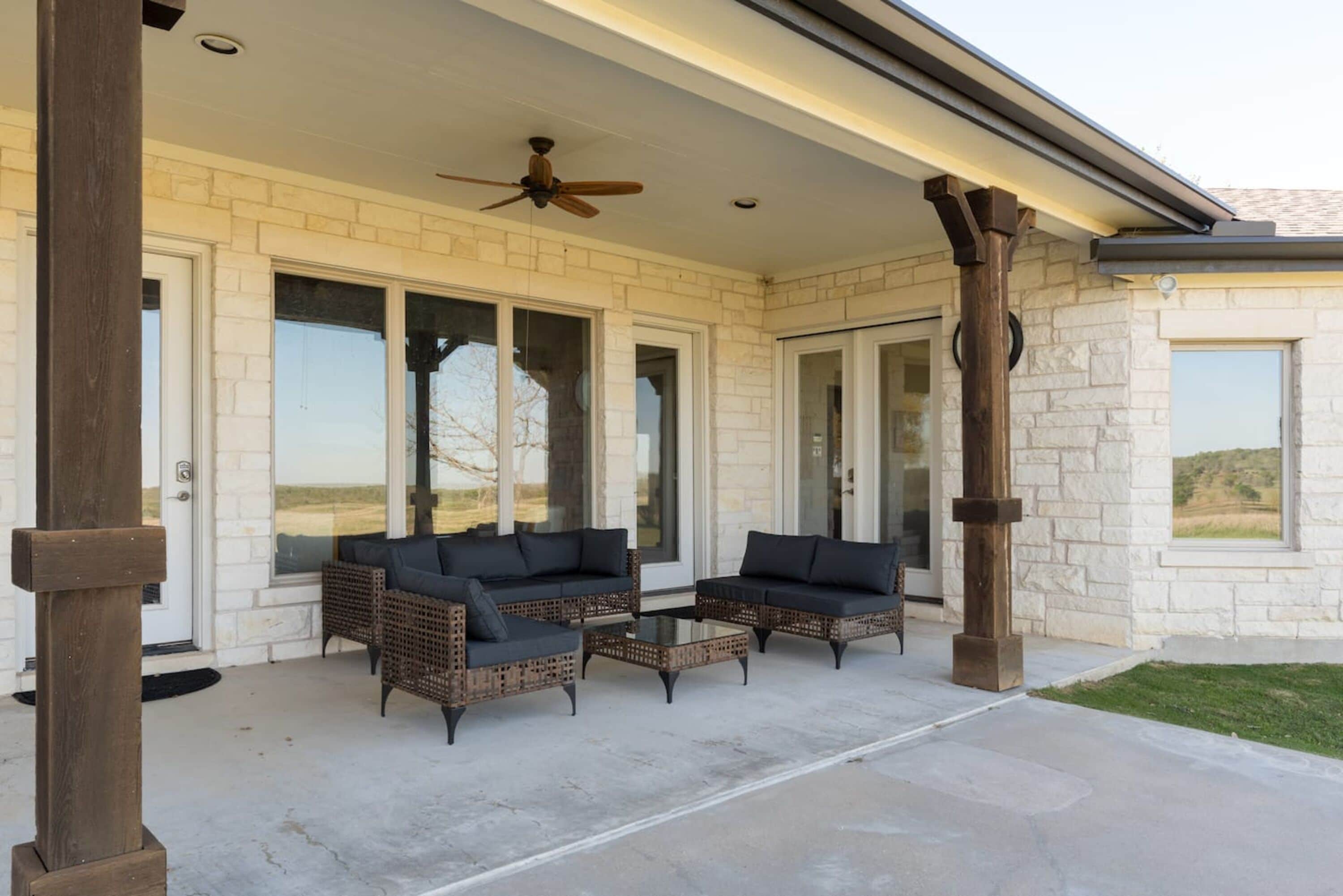 A covered patio area with two sofas and a table, a ceiling fan, and a view of the landscape.