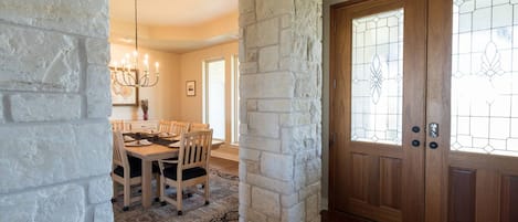 A dining area with a table set for four, a chandelier, and a stone wall.