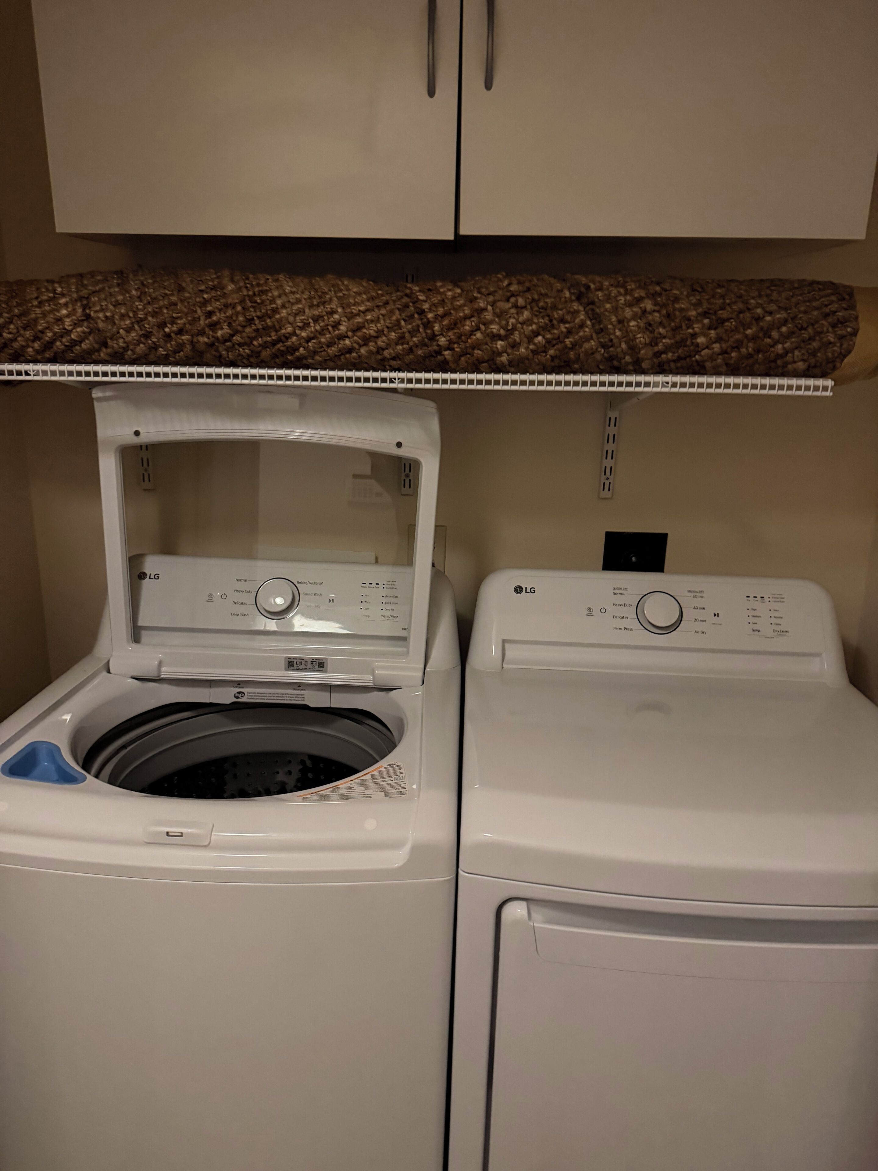 A laundry area with a front-loading washer and dryer, a control panel, and a woven shelf above.
