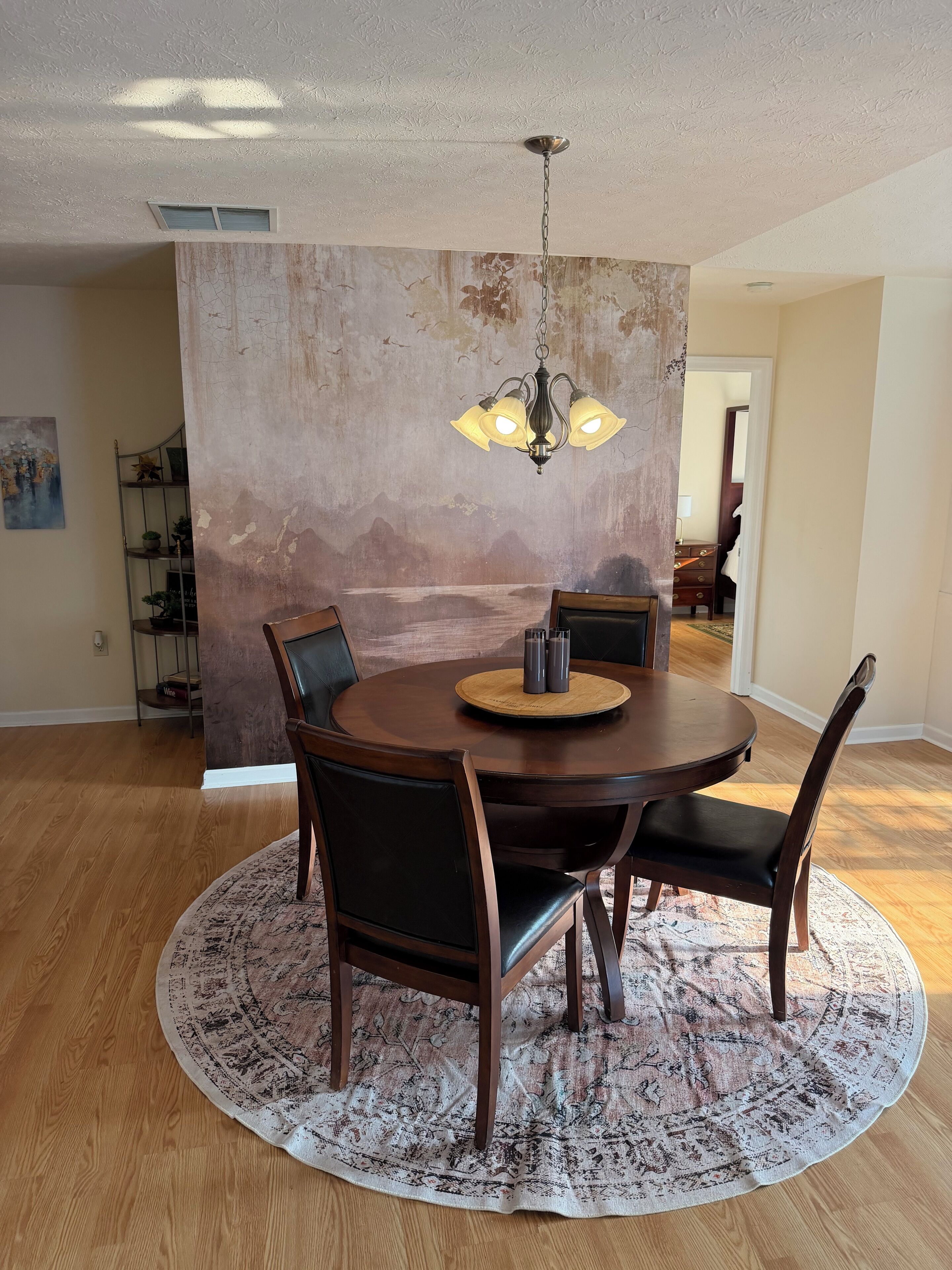 A dining area with a round table, chairs, a chandelier, and a textured wall.