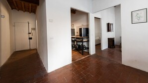 Ein Flur mit Fliesenboden, einer weißen Tür und einem Küchenbereich mit Kühlschrank und Regalen.