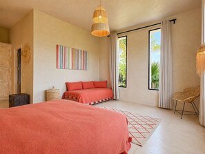 A bedroom with a large bed, a bedside table, a lamp, a window with curtains, and a wall art piece. - Palais Samalya (Bouzama)