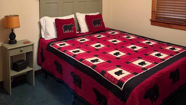 Ein Schlafzimmer mit Bett, Nachttisch, Lampe, Deckenventilator und einem Fenster mit Jalousien.