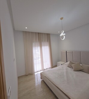 A modern bedroom with a large bed, a nightstand, a bedside table, and a hanging light fixture.