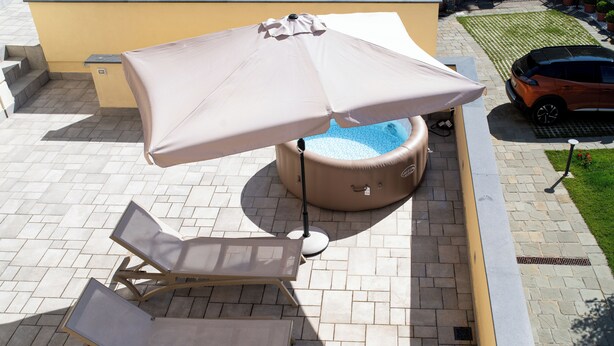 A patio area with a hot tub, lounge chairs, and an umbrella. - De Vivo Realty - Villa Colomba (Ticciano)