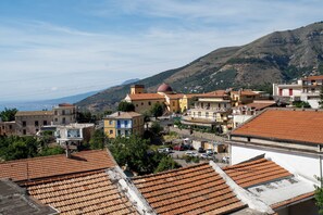 A coastal town with terracotta-roofed buildings, a prominent church with a dome, and a view of the sea and mountains in the background. - De Vivo Realty - Villa Colomba (Ticciano)