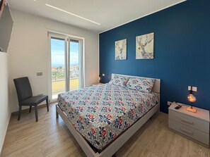 A bedroom with a bed, a chair, a nightstand, and artwork on the wall. - De Vivo Realty - Villa Colomba (Ticciano)