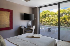 Habitación de hotel con cama, escritorio con televisor de pantalla plana, silla y vista a una piscina y palmeras.