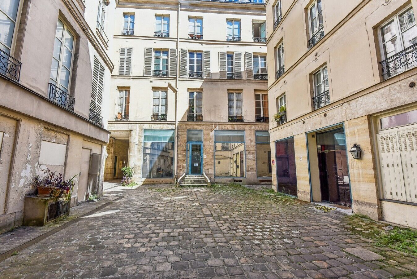 A courtyard with cobblestone pavement, a central entrance with steps, and buildings with balconies and windows.