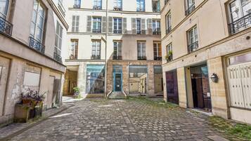 A courtyard with cobblestone pavement, a central entrance with steps, and buildings with balconies and windows.